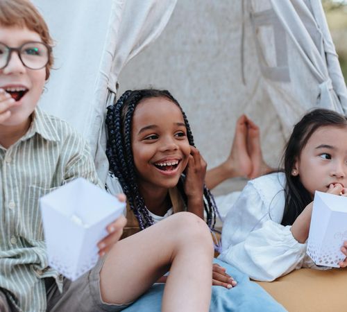Group of diverse children laughing while doing simple stretches on mats.